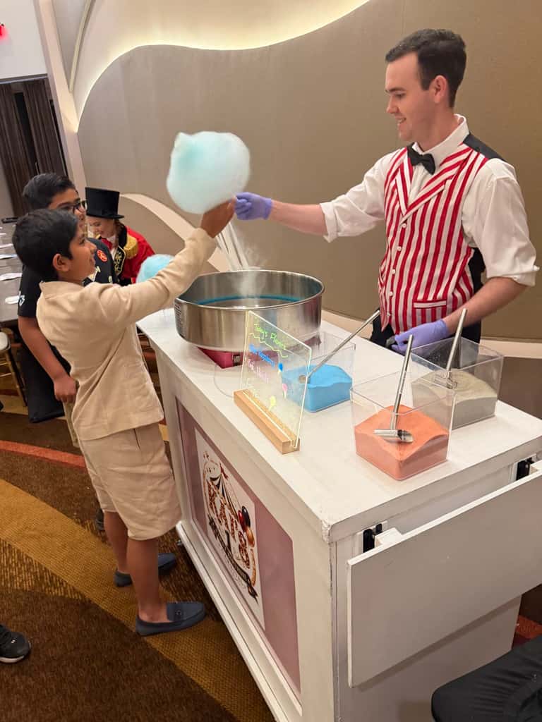 A striped-vest attendant spins fresh cotton candy at a circus-style confection cart
