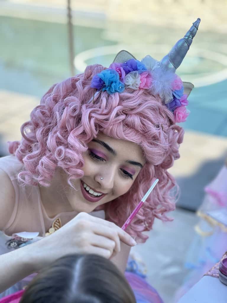 A unicorn performer paints a young guest's face