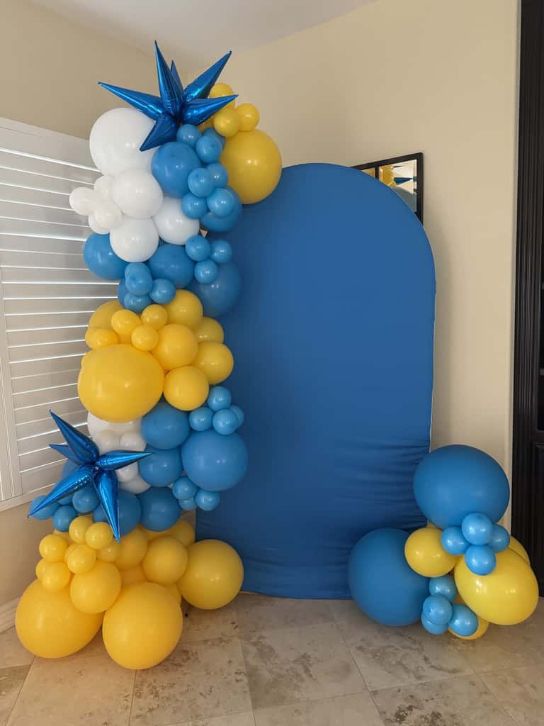 A blue and yellow balloon garland framing a backdrop arch, with foil stars
