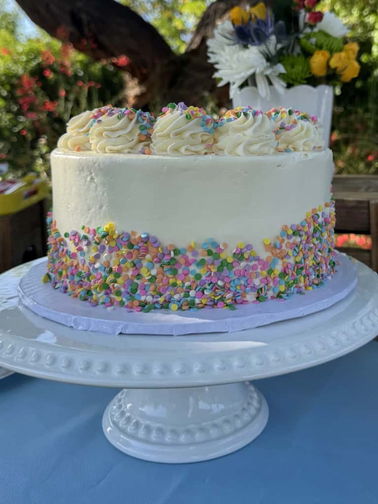 An eight-inch confetti cake with buttercream rosettes and pastel sprinkles on a white stand