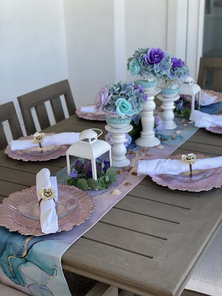 A sculpted table centerpiece of roses and hydrangea over a shell-strewn runner