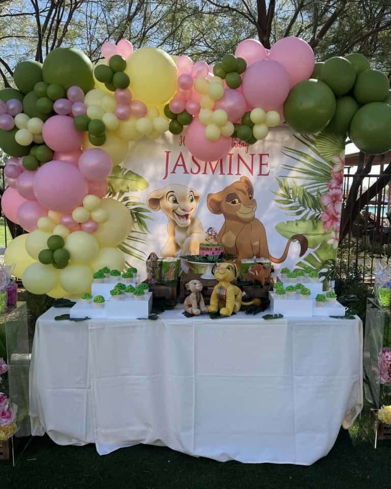 A jungle-themed dessert table under a pink, green, and yellow organic balloon garland arch