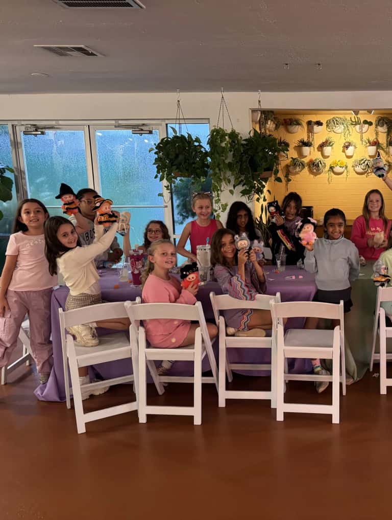 Young guests seated at the kids tables in white folding chairs, holding their craft dolls