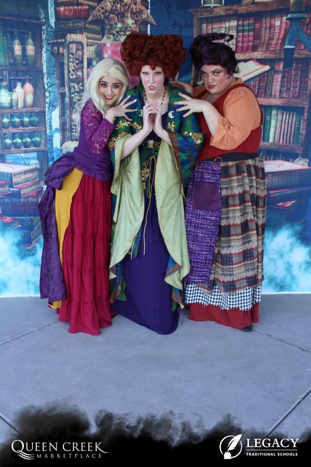 The three Sanderson sisters from Hocus Pocus pose against an apothecary backdrop