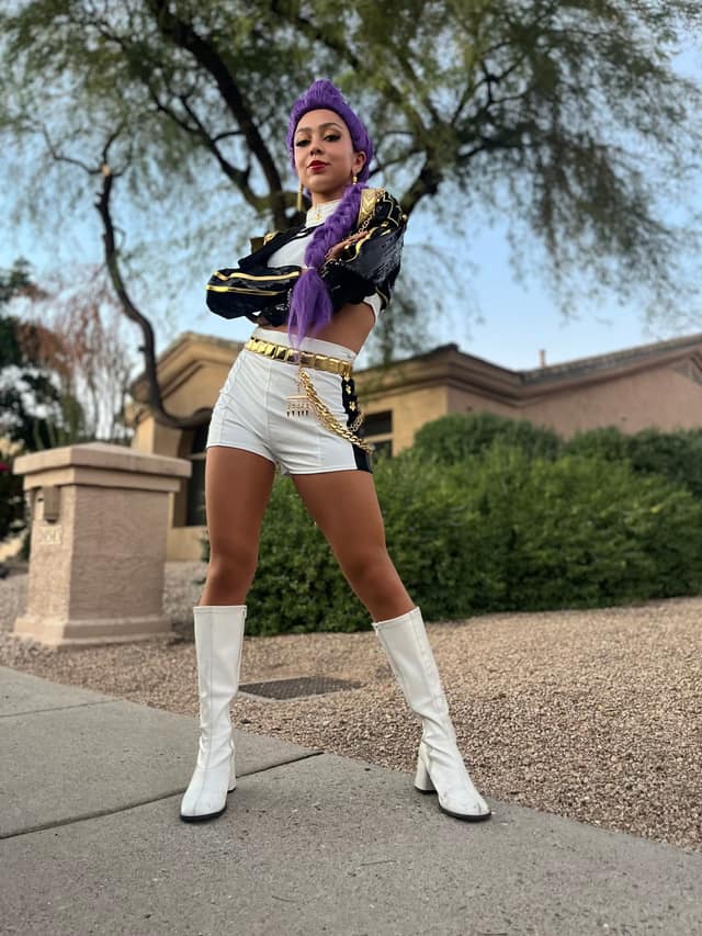 A performer in a bold white-and-gold stage costume poses outdoors