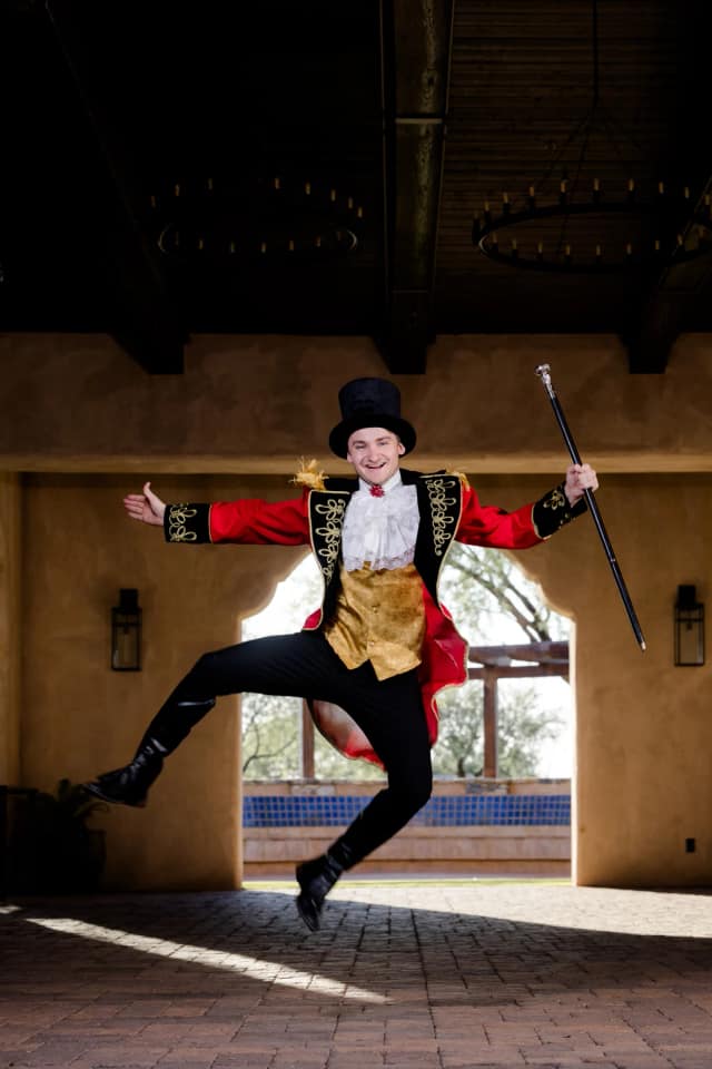 A ringmaster performer in a red tailcoat and top hat leaps mid-air with a cane
