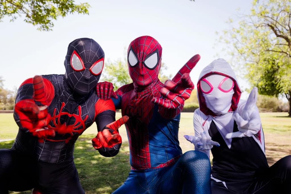 Three Spider-Man characters, including Spider-Gwen, pose together outdoors